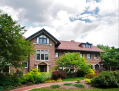 Cheney Mansion, a two-story brick building with a red tile roof, surrounded by lush green trees and gardens.